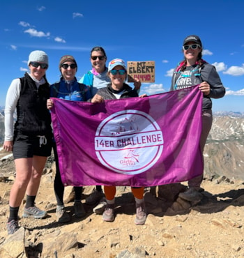 5 people hold a large pink flag with 14er Challenge on it.